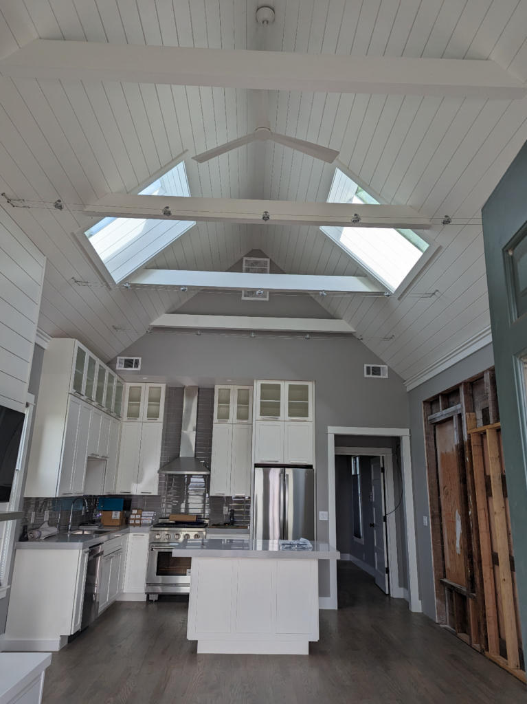 An airy kitchen remodel with high ceilings, white and gray cabinets, state of the art appliances, and custom lighting fixtures.