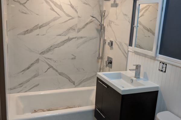 bathroom-remodel-2 A beautiful bathroom remodel with a modern black vanity, white wooden siding and dark charcoal paint, plus decorative gray and white floor tiles, and marble patterned tiles in the shower.