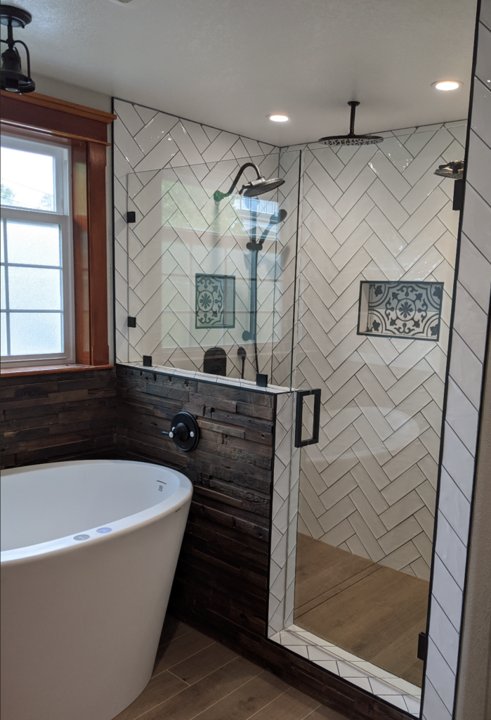 A beautiful remodeled bathroom in the Victorian house with white subway tile in the shower, glass doors, a deep bath, black and white tile details, and black hardware throughout.