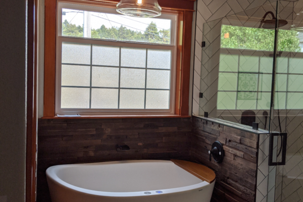 cozy-bath A cozy bathroom remodel with a deep bathtub, warm lighting, expertly laid subway tiles, dark wooden accents, and new black hardware.
