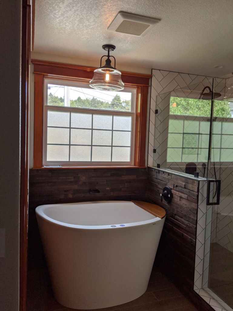 A cozy bathroom remodel with a deep bathtub, warm lighting, expertly laid subway tiles, dark wooden accents, and new black hardware.