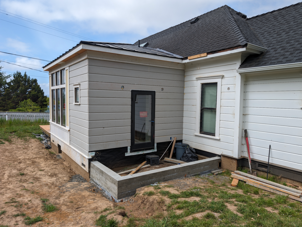 The back side of the addition to the Shotgun House showing fresh siding, a new glass door, and an area for a new deck.
