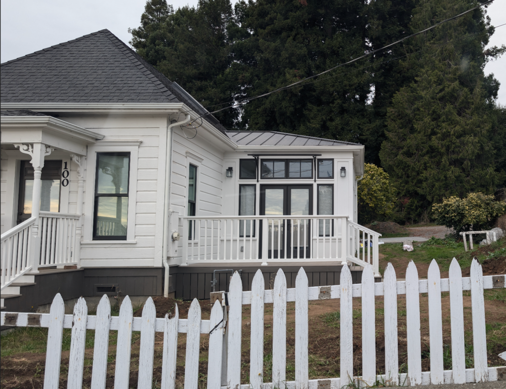 Street view of the historic Shotgun house remodel with the completed addition painted white, with black trim windows, and a deck.
