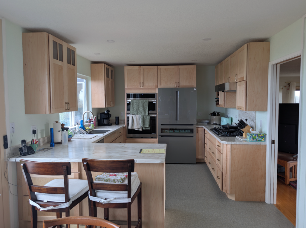 A client's kitchen after their Ultimate Building Solutions remodel showcasing fresh granite countertops, a new high end range, state of the art appliances, light wooden cabinets, and a completely redesigned layout optimizing space for the family.