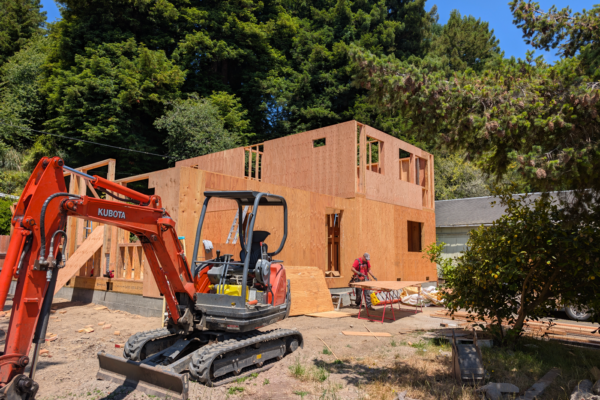 new-construction A excavator helps clear the foundation for a new house built by Ultimate Building Solutions. The house is starting to shape with wooden framing as a worker prepares the next pieces.