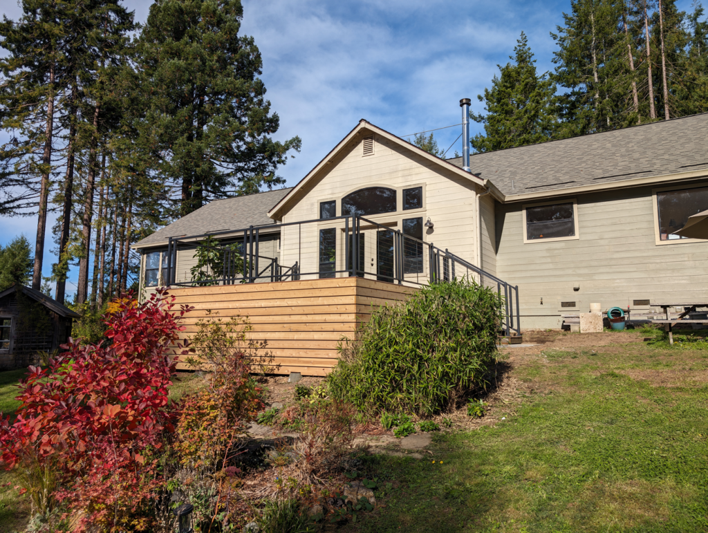 A beautiful, sunny deck built on a hillside in front of a one-story house with large windows.