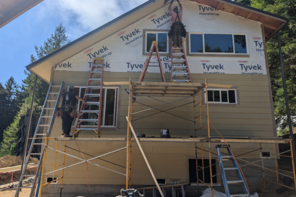 working A worker stands on a ladder on top of scaffolding to add siding to the second story of a newly built house on a sunny day.