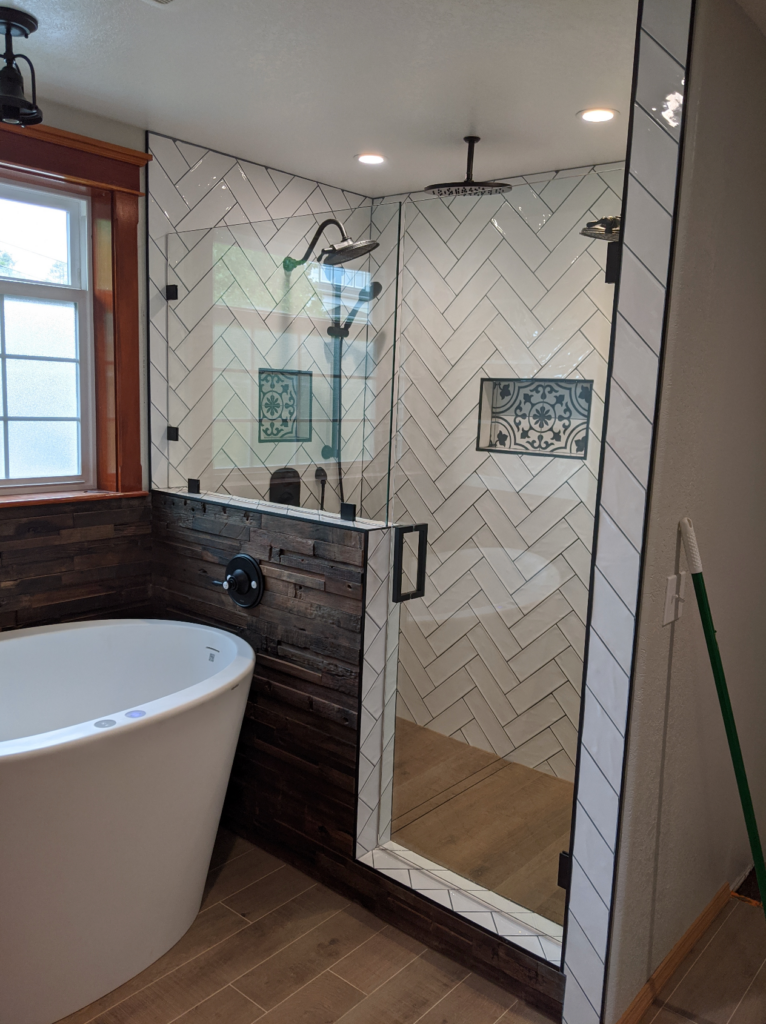 A beautiful remodeled bathroom in the Victorian house with white subway tile in the shower, glass doors, a deep bath, black and white tile details, and black hardware throughout.
